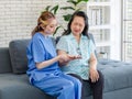 Asian young professional female doctor in blue hospital uniform sitting on sofa couch helping old chubby retirement pain palm in