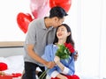 Asian young romantic cheerful lover couple male boyfriend sitting on bed giving red roses bouquet kissing surprise female Royalty Free Stock Photo