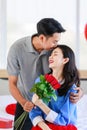 Asian young romantic cheerful lover couple male boyfriend sitting on bed giving red roses bouquet kissing surprise female Royalty Free Stock Photo