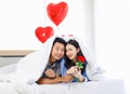 Asian young romantic lover couple male boyfriend giving red rose surprising female girlfriend laying down under blanket on bed