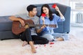 Asian young romantic lover couple male boyfriend sitting on carpet floor in living room playing guitar singing song while female Royalty Free Stock Photo