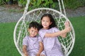 Asian young sister and little brother looking at each other and sitting together on the white cradle in the garden. Boy and girl Royalty Free Stock Photo