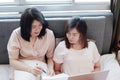 Asian young sisters lovely couple laying on white bed and talking together for online working with laptop in bedroom. Royalty Free Stock Photo