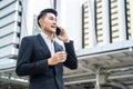 Asian young smart businessman talking telephone in city. The man holding phone and coffee walking outdoor to working office with s Royalty Free Stock Photo