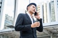 Asian young smart businessman talking telephone in city. The man holding phone and coffee walking outdoor to working office with s Royalty Free Stock Photo