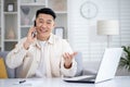 Asian young smiling male freelancer working at home, sitting at the table and talking emotionally on the mobile phone Royalty Free Stock Photo