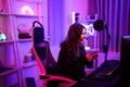 Asian young streamer girl playing esports game online while talking with her team by microphone and headset gadget in neon light