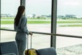 Asian young traveler woman at airport wearing face mask standing with luggage looking the airport gate windows at planes on airpor Royalty Free Stock Photo