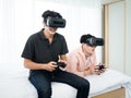 Asian young two boy immerse playing video game by virtual reality headset and joystick controller gadget on bed in white bedroom Royalty Free Stock Photo