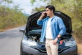 Asian young unhappy man talking on a cell phone  in front of the open hood  broken down car On Country Road Phoning For Help. Royalty Free Stock Photo