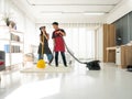 Asian young wife cleaning and singing with yellow twist mob and husband looking at her while using vacuum cleaner on the floor in Royalty Free Stock Photo