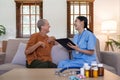 Asian young woman caregiver doctor give consultation and writing problem of elderly woman patient in room during home Royalty Free Stock Photo