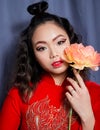 Asian Young Woman Close-up, in Red Wedding Dress, With Graphic Red Make-up and a Orange Flower in her Hand, on Blue Background Royalty Free Stock Photo