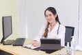 Asian young woman doctor in a white lab coat is sitting on office room at hospital while has a computer, clipbroad and alcohol gel Royalty Free Stock Photo