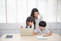 Asian young woman help her son do homework with daughter using laptop sit beside on table in living room at home Royalty Free Stock Photo