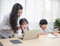 Asian young woman help her son do homework with daughter using laptop sit beside on table in living room at home Royalty Free Stock Photo