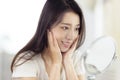 Asian young woman looking at her face in mirror Royalty Free Stock Photo