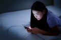 Asian young woman lying on the white bed and playing smartphones during night time Royalty Free Stock Photo