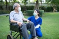 Asian young woman nurse at nursing home take care and support disabled senior elderly man on wheelchair at backyard. Caregiver