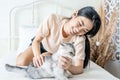 Asian young woman play with the fur little cat with happiness at home. Beautiful female sit on bed, spend leisure time stroking Royalty Free Stock Photo