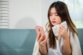 woman sick sitting down on sofa with cold blowing her nose and checking smart mobile phone Royalty Free Stock Photo