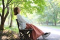 Asian young woman sitting bench look up under green tree in park on sunny day Royalty Free Stock Photo