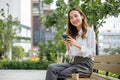 Asian young woman sitting on bench outdoor on park using smart mobile phone Royalty Free Stock Photo
