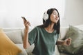 Asian young woman sitting on sofa. Happy female listening music and dancing in living room Royalty Free Stock Photo