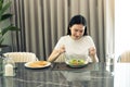 Asian young woman smiling as she scoops a salad on a plate and eats happily at home