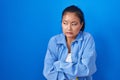 Asian young woman standing over blue background shaking and freezing for winter cold with sad and shock expression on face Royalty Free Stock Photo