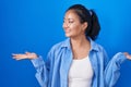 Asian young woman standing over blue background smiling showing both hands open palms, presenting and advertising comparison and Royalty Free Stock Photo