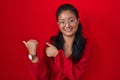 Asian young woman standing over red background pointing to the back behind with hand and thumbs up, smiling confident Royalty Free Stock Photo