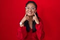 Asian young woman standing over red background smiling with open mouth, fingers pointing and forcing cheerful smile Royalty Free Stock Photo