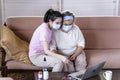 Asian young woman teach elder mother, how to wear face mask from online learn in living room with carefully. family concept