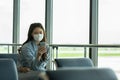 Asian young woman traveller wearing face maks using mobile phone at airport Due Covid-19 flu virus pandemic