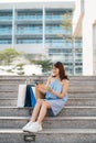 Asian young woman using phone and holding credit card to purchase while sitting on stairs with color shopping bags Royalty Free Stock Photo