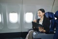 Asian young woman using tablet sitting near windows at first class on airplane during flight, Traveling and Business Royalty Free Stock Photo