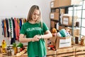 Asian young woman wearing volunteer t shirt at donations stand checking the time on wrist watch, relaxed and confident