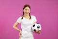 Asian Young woman in white t-shirt over isolated pink background holding a soccer ball and looking at camera Royalty Free Stock Photo