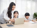 Asian young woman help her son do homework with daughter using laptop sit beside on table in living room at home Royalty Free Stock Photo