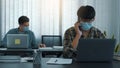 Asians sit in their office and use the phone to talk to clients while wearing masks in their offices during COVID-19