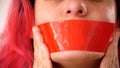 Close-up female face. Red tape sealed mouth. Serious woman with her lips covered by a tape.