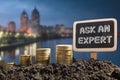 Ask an expert. Financial opportunity concept. Golden coins in soil Chalkboard on blurred urban background Royalty Free Stock Photo