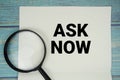 Ask Now text written on notepad with magnifying glass flat lay on wooden background Royalty Free Stock Photo