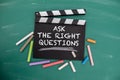 Ask The Right Questions. Black movie clapper with chalk pieces on a green chalkboard background