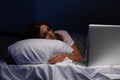 Asleep young internet addict woman in the bed with laptop.