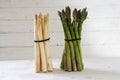 Asparagus, a green and a white bunch stand on a white painted wooden background, copy space