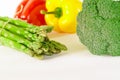 Asparagus, Juicy red and orange peppers with a green tail lies next to Bundle of lettuce and broccoli are on a white background Royalty Free Stock Photo