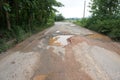 The road is full of potholes and waterlogged. The old asphalt road surface is rough and bumpy and in need of repair.