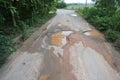 The road is full of potholes and waterlogged. The old asphalt road surface is rough and bumpy and in need of repair.